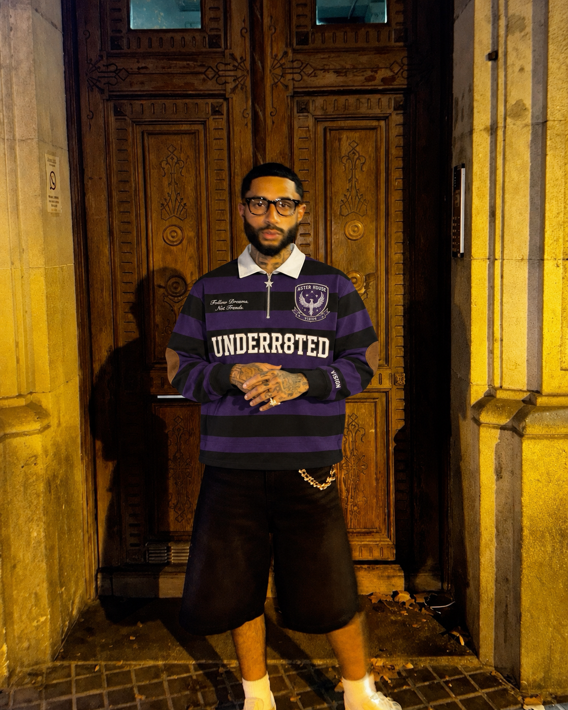 A student in a purple Aster rugby shirt standing before the tall wooden doors of the main hall