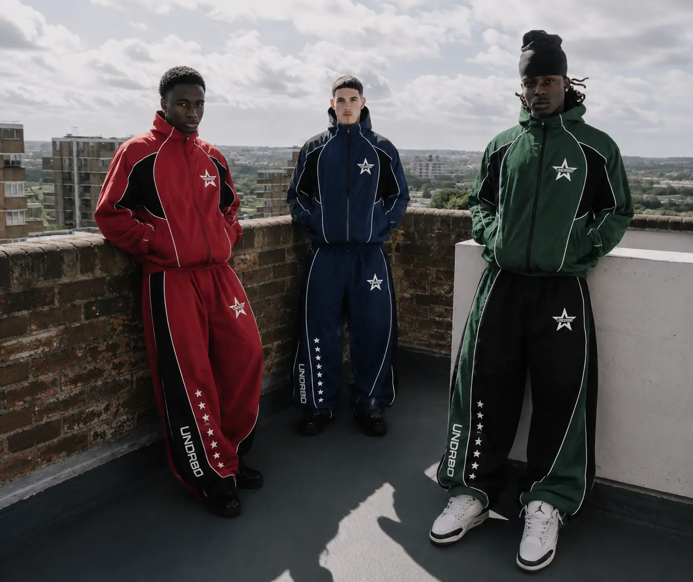 Three students in crimson, navy and green House tracksuits on a campus rooftop at dusk