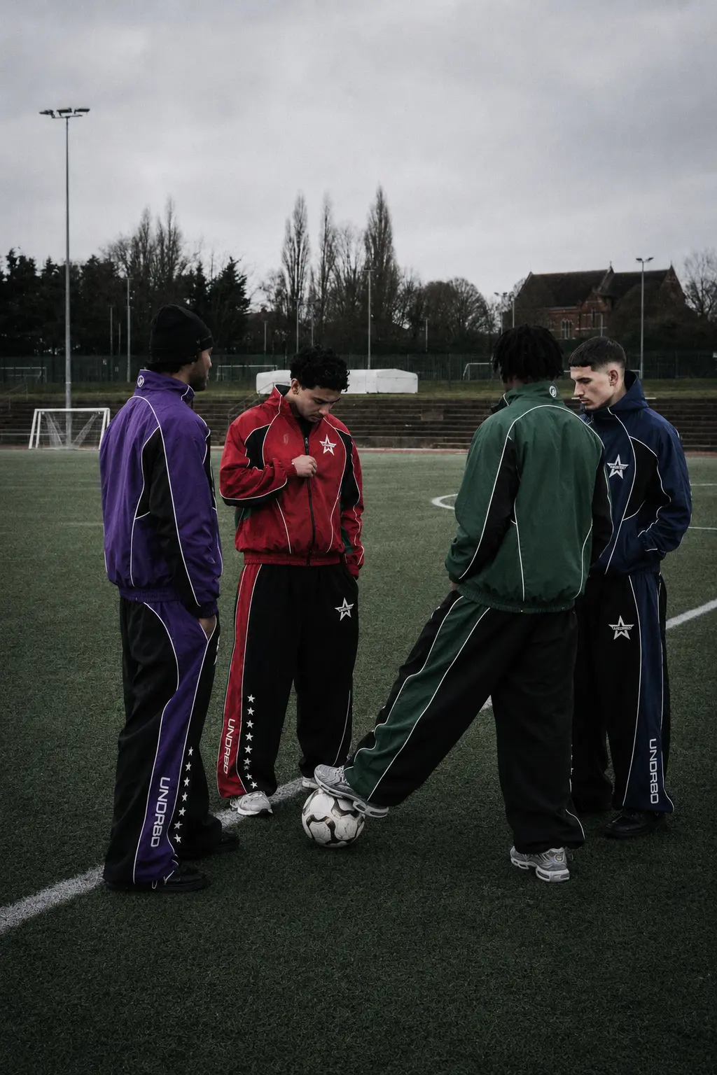 Four students in purple, crimson, green and navy House tracksuits standing together on the campus field
